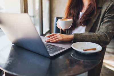 Midsection of woman drinking coffee cup on table