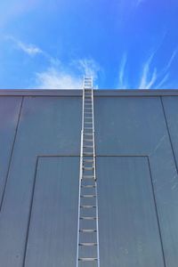 Low angle view of ladder by wall against sky