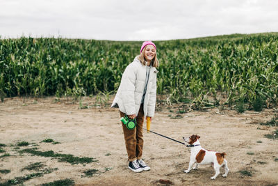 Cheerful teenage girl playing in the field with her dog jack russell terrier on the background