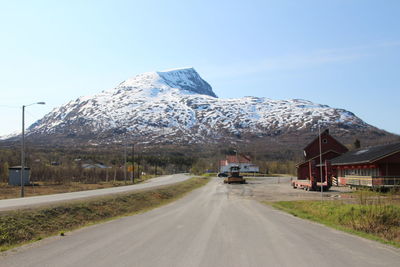 Road by snowcapped mountains against clear blue sky