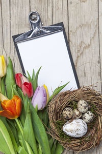 High angle view of colorful eggs and flowers with note pad on table