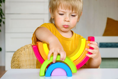 Little blond hair boy in clothes made of natural fabric plays with rainbow colored wooden toys at