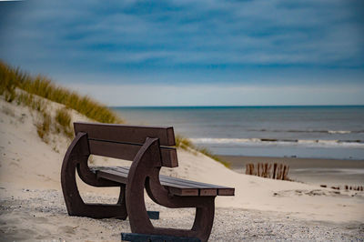 Empty bench on beach by sea against sky