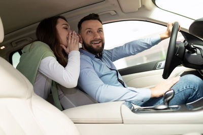 Woman whispering man sitting in car