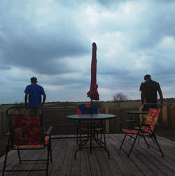 Rear view of men sitting on table against sky