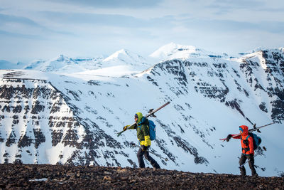 Man and woman walking on rocks with skis with mountains behind