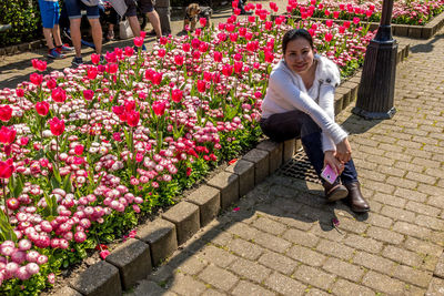 Portrait of smiling woman sitting by flowers in park