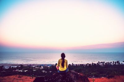 Rear view of woman sitting on beach against clear sky