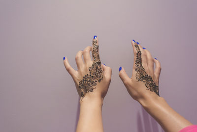 Cropped hands of woman with henna tattoo by wall