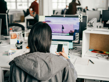 Rear view of businesswoman using mobile phone in office