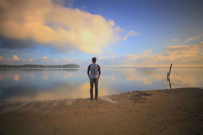 Rear view of man standing at beach against sky during sunset