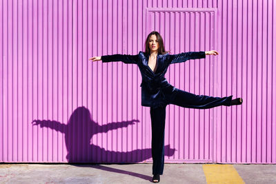 Full length of woman with arms outstretched standing against pink wall