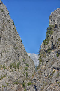 Low angle view of rocky mountains against clear blue sky