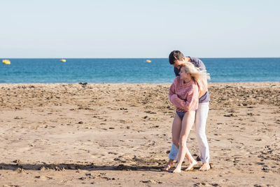 Happy young couple romancing at sandy beach during sunny day