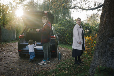 Father and mother with daughter standing near electric car during sunny day