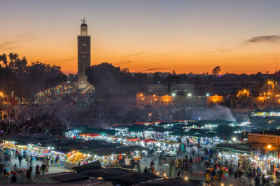 Crowd at illuminated city during sunset