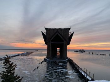 Built structure on beach against sky during sunset