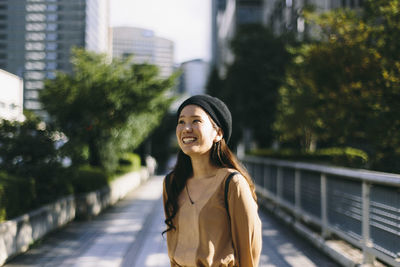 Portrait of smiling young woman standing by trees in city