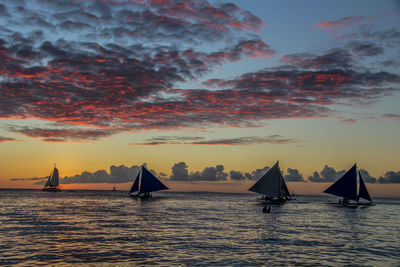 Sailboats sailing in sea against sky during sunset