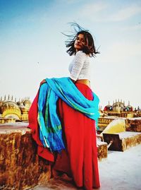 Woman looking away while standing against blue sky