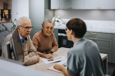 Senior couple discussing with interior designer over brochure while sitting at desk in store