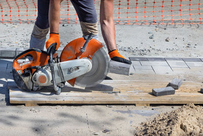 A worker cuts paving slabs with a diamond blade and a gas cutter on a clear summer day.