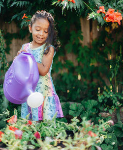 Diverse mixed race pre school girl outdoors during summer watering plants in garden