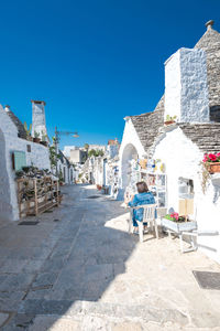 Rear view of man walking on street against clear blue sky