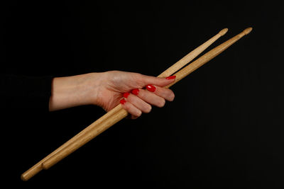 Cropped hand of woman holding chopsticks against black background