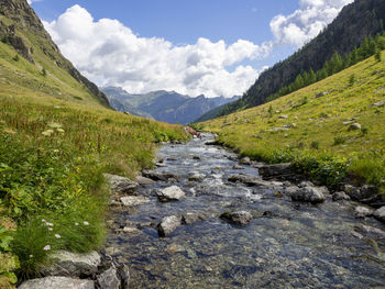 Scenic view of stream amidst green landscape against sky