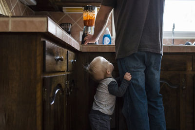 Side view of boy standing by father working in kitchen