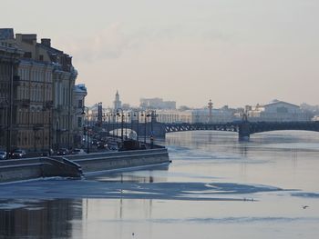 Bridge over river by buildings in city against sky