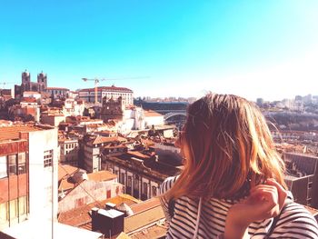 Young woman wearing sunglasses while standing against cityscape during sunny day