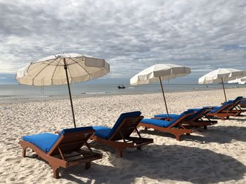 Lounge chairs and parasols on beach against sky