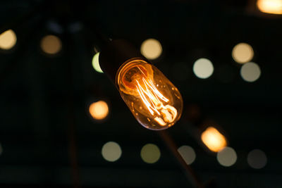 Low angle view of illuminated light bulb hanging against black background