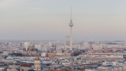 Fernsehturm amidst cityscape against sky during sunset