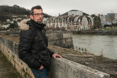 Portrait of young man standing by canal during winter