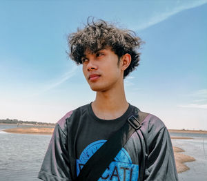 Portrait of young man looking away at beach against sky