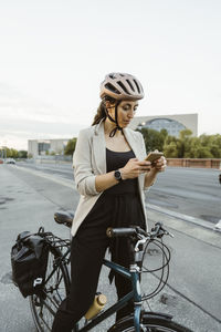 Businesswoman using smart phone while standing with bicycle at street in city