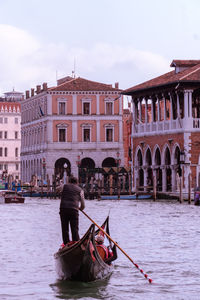 Rear view of man rowing while standing on boat in canal against sky