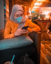 Young woman using mobile phone while sitting in kitchen