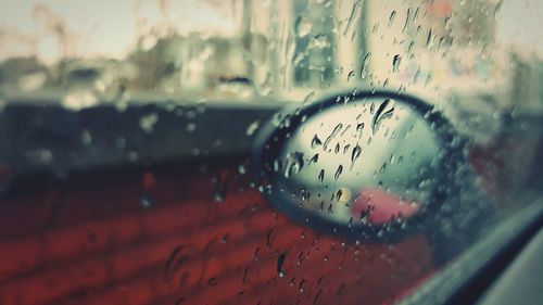 Close-up of side-view mirror seen from wet window