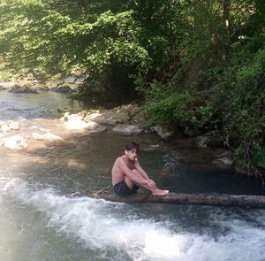 Young man in river against trees in forest