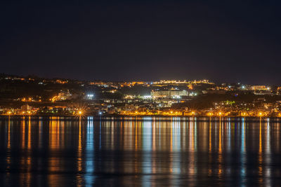 Illuminated buildings by river against sky at night