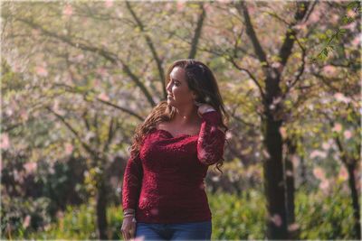 Woman looking away while standing against trees in park