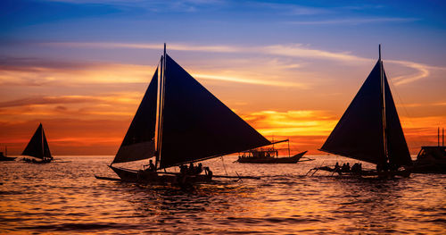 Boats sailing in sea at sunset