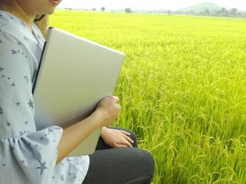 Midsection of woman holding laptop while sitting at farm
