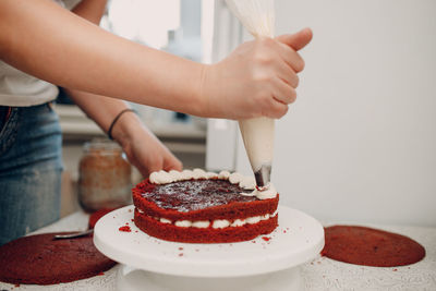 Woman piping cream on red velvet cake at home