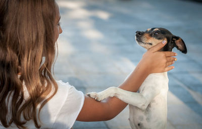 Side view of woman pampering dog on footpath