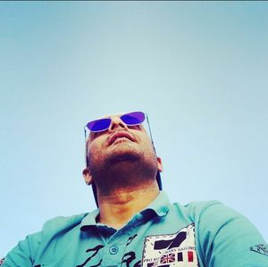 Low angle view of man wearing sunglasses against clear blue sky
